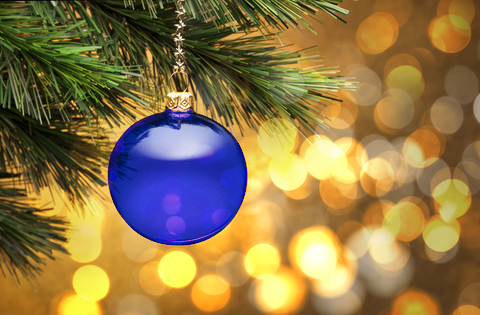 A blue glass bauble hanging from a pine tree branch