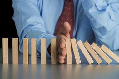 A businessman stopping a line of blocks from falling using his hand